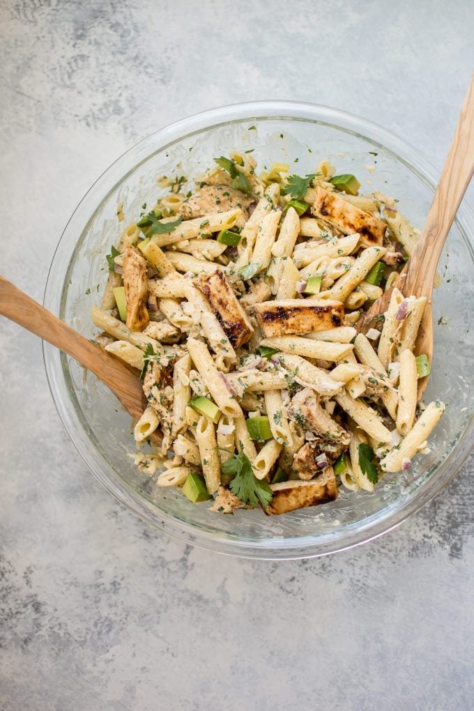 glass bowl with healthy grilled chicken pasta salad and wooden salad utensils
