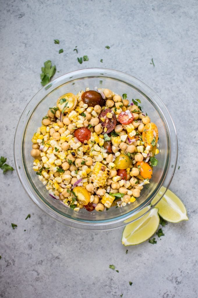 glass bowl of summer grilled corn and chickpea salad with lime wedges