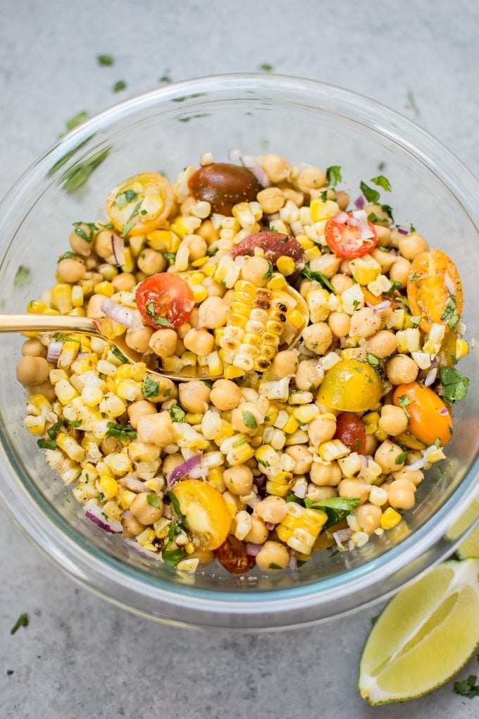 close-up of grilled corn chickpea salad in a glass bowl with a serving spoon