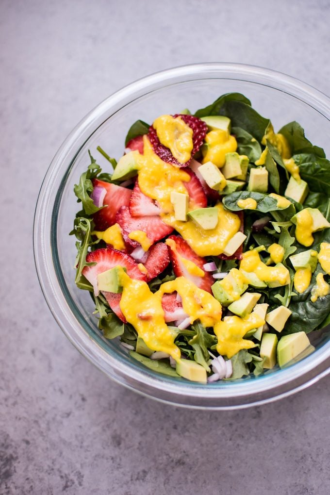 glass bowl with salad greens, avocado, and strawberries drizzled with easy homemade mango dressing