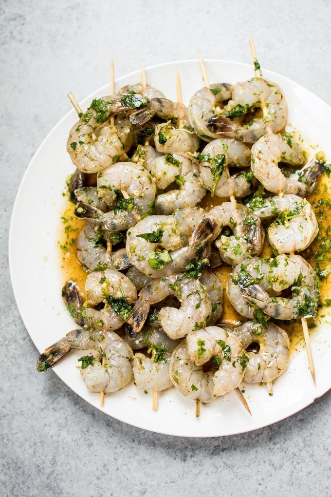 several raw shrimp on wooden skewers in tequila marinade on a white plate