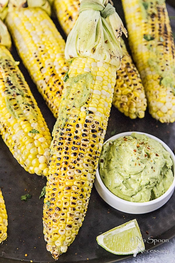 several ears of grilled corn next to avocado sriracha dipping sauce