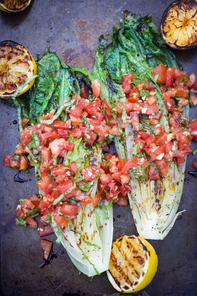 two grilled romaine lettuce heads with tomatoes and lemon