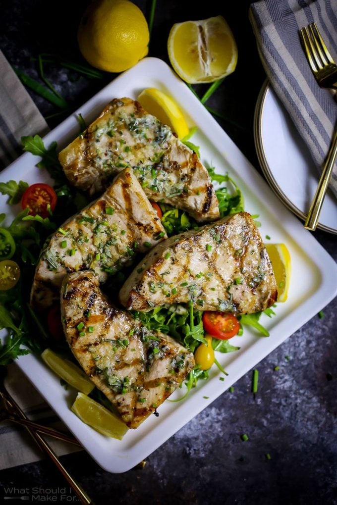 grilled swordfish pieces on a white square plate with lemon wedges and a fork