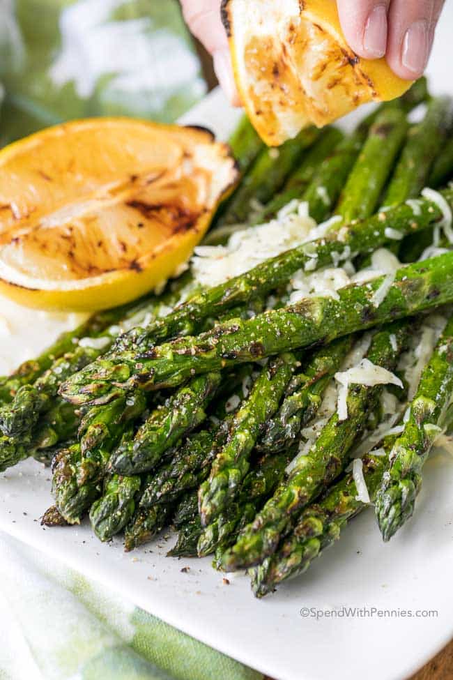 a hand squeezing lemon on a stack of grilled asparagus