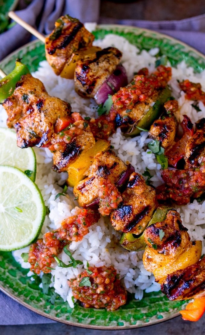 two mexican chicken skewers over a bed of rice with salsa and lime