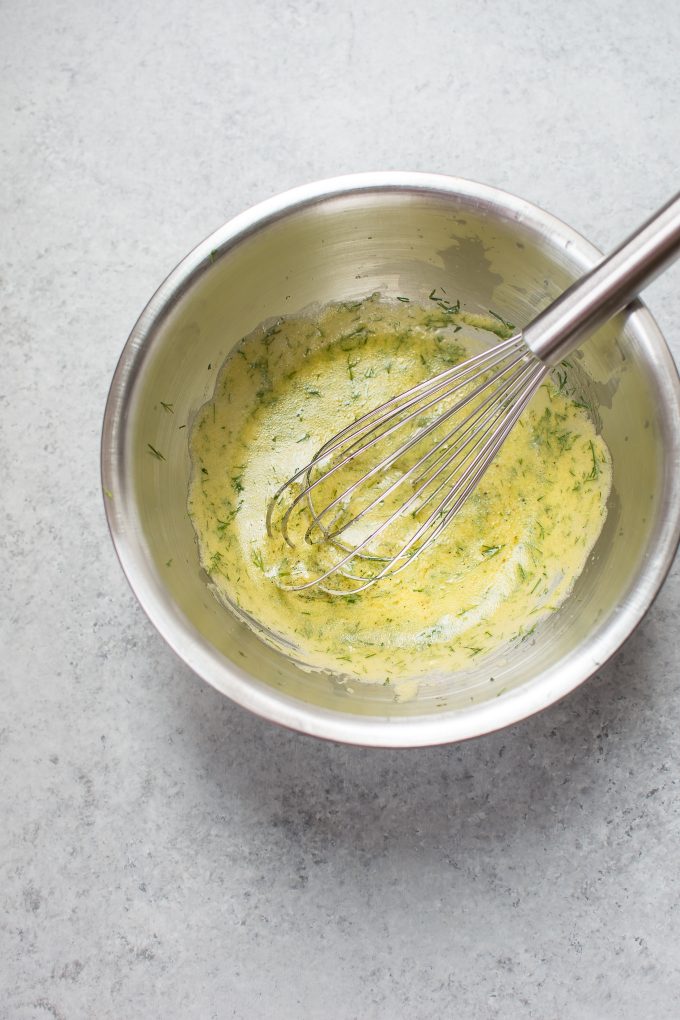 metal mixing bowl with lemon dill dressing and whisk