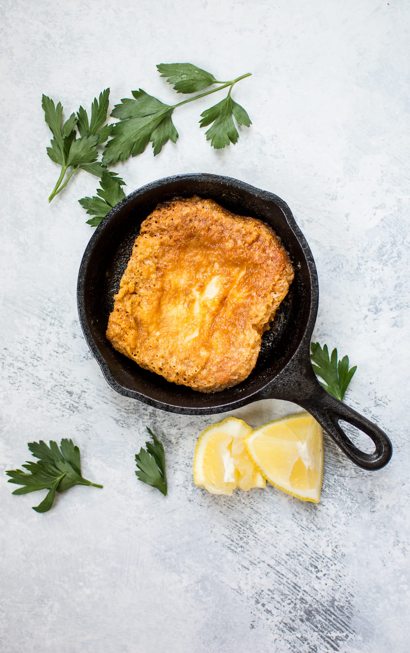 tiny cast iron skillet with Greek fried cheese beside parsley and lemon wedges
