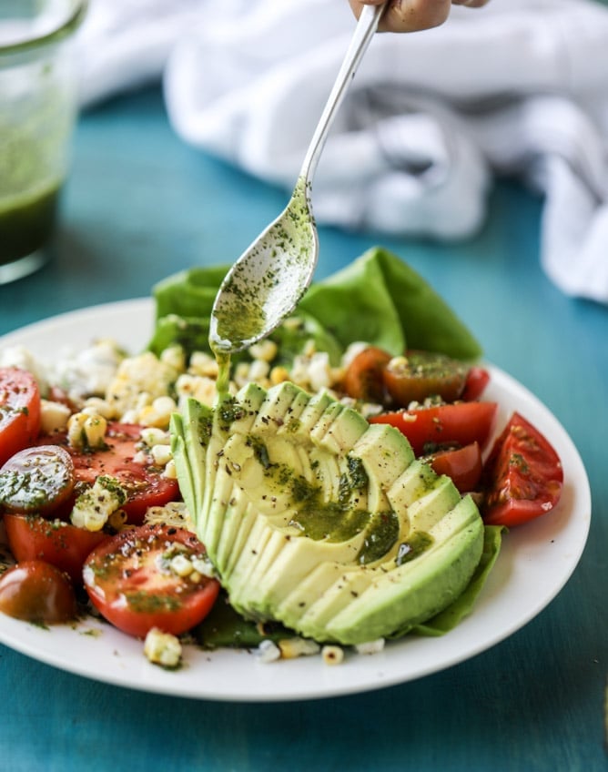 grilled corn, tomato, and avocado salad on a plate with chimichurri dressing on a spoon