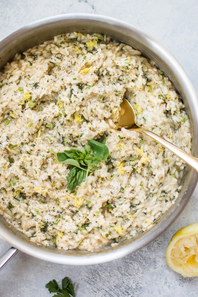 skillet with lemon herb risotto and serving spoon beside half a lemon