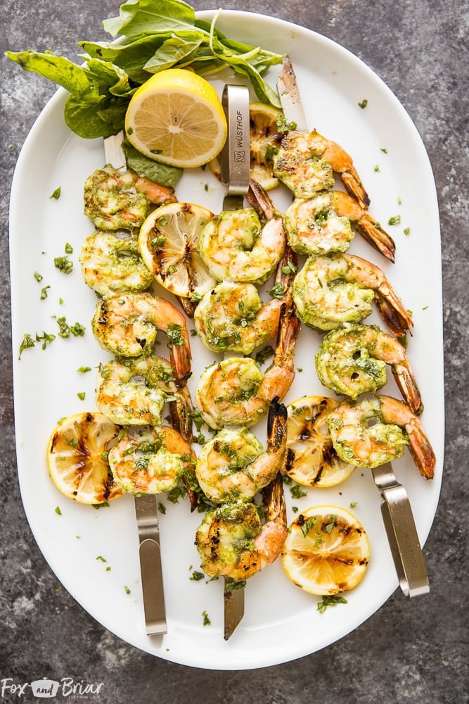 three pesto grilled shrimp skewers on an oval plate with lemon