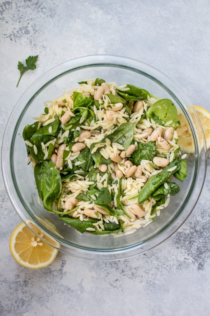 glass bowl with spinach orzo salad and lemon wedges