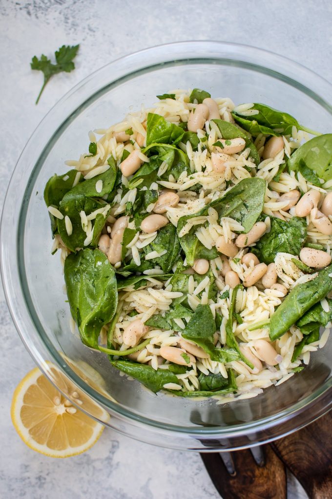 close-up of glass bowl with spinach orzo salad with white beans
