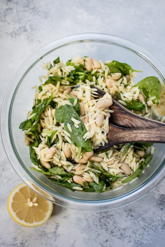 glass bowl with spinach white bean salad with orzo and wooden salad utensils