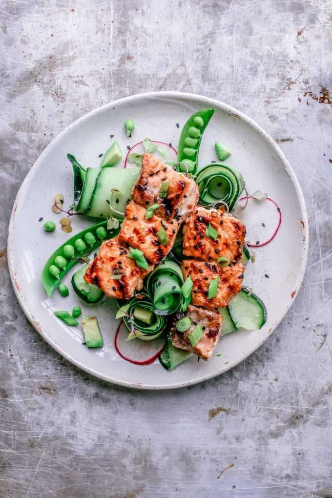 sweet chili salmon skewers on a white plate with sugar peas