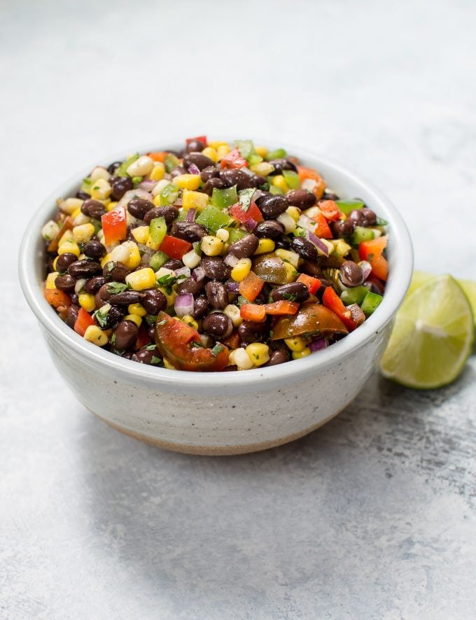 white bowl with corn and black bean salad beside lime wedges