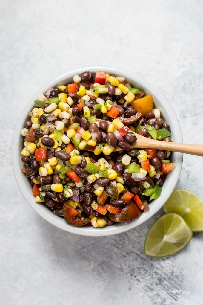white bowl with black bean and corn salad with wooden serving spoon and lime wedges