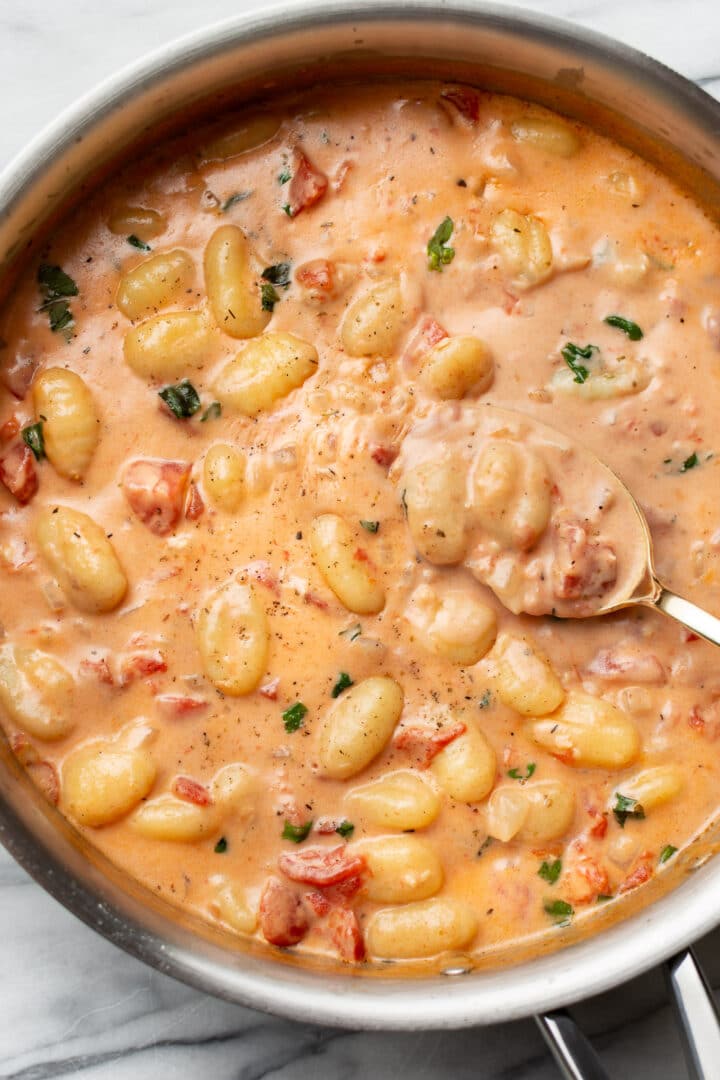 a skillet with creamy tomato gnocchi and a serving spoon