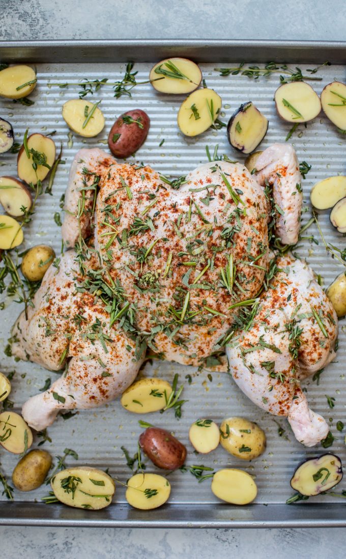 spatchcock chicken and potatoes on baking sheet ready for the oven