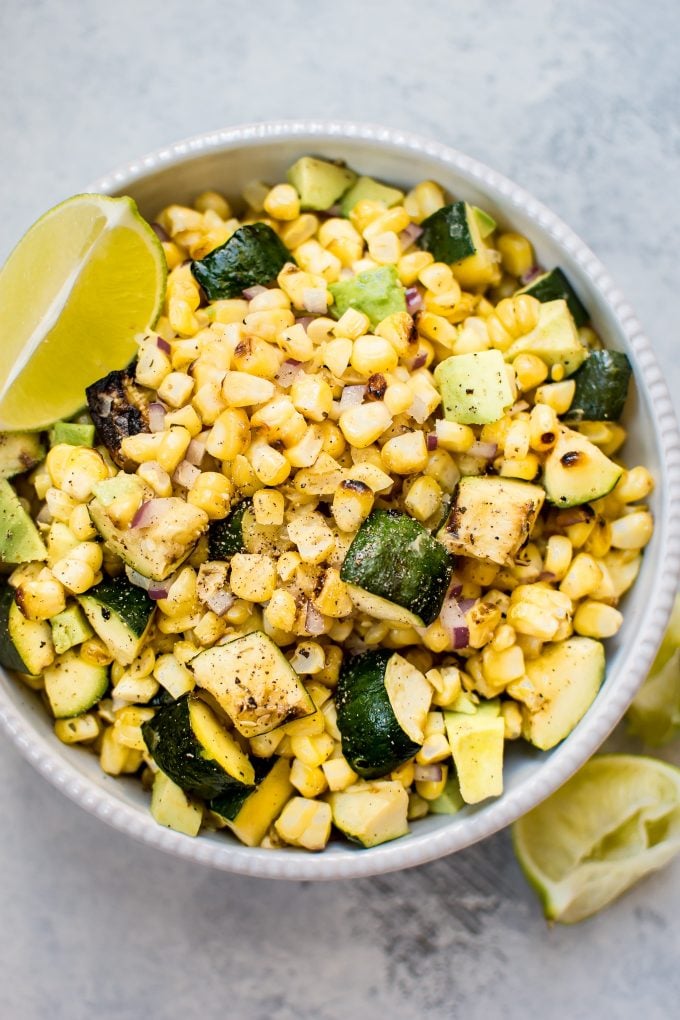 grilled corn and zucchini salad in a bowl with lime wedge