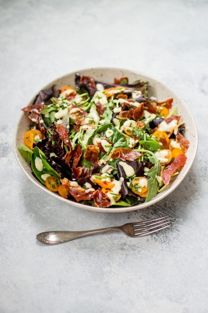 bowl of mixed greens salad with prosciutto beside a fork