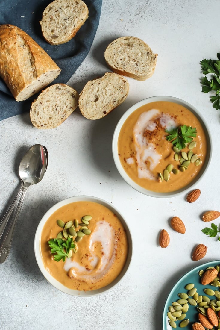 two bowls of almond butter pumpkin soup with baguette slices and spoons