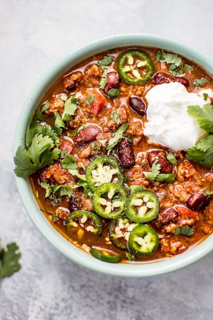 teal bowl with Crockpot turkey chili topped with Greek yogurt, cilantro, and sliced jalapeno peppers