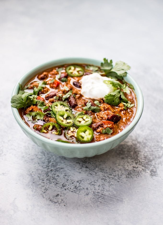 teal bowl of slow cooker turkey and bean chili with cilantro and sliced jalapenos