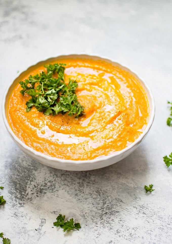 carrot celeriac soup in a white bowl topped with parsley