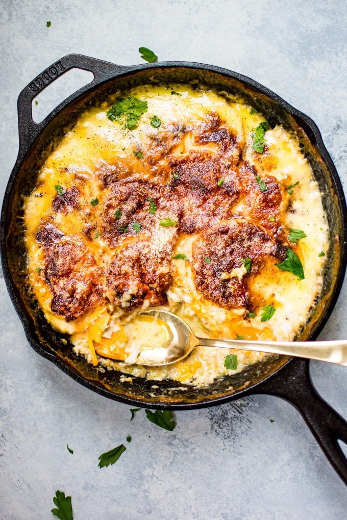 cheesy scalloped sweet potatoes in a cast iron skillet with a serving spoon