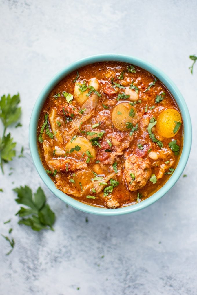 teal bowl with slow cooker cabbage soup with beans, sausage, and potatoes