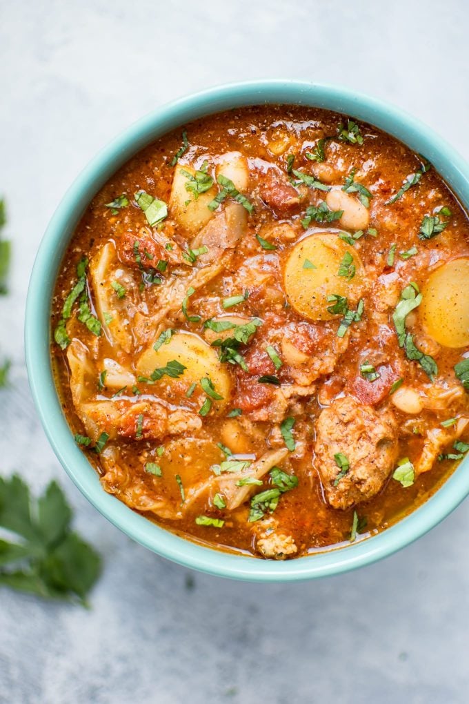 Crockpot cabbage soup with potatoes, beans, and sausage in a teal bowl