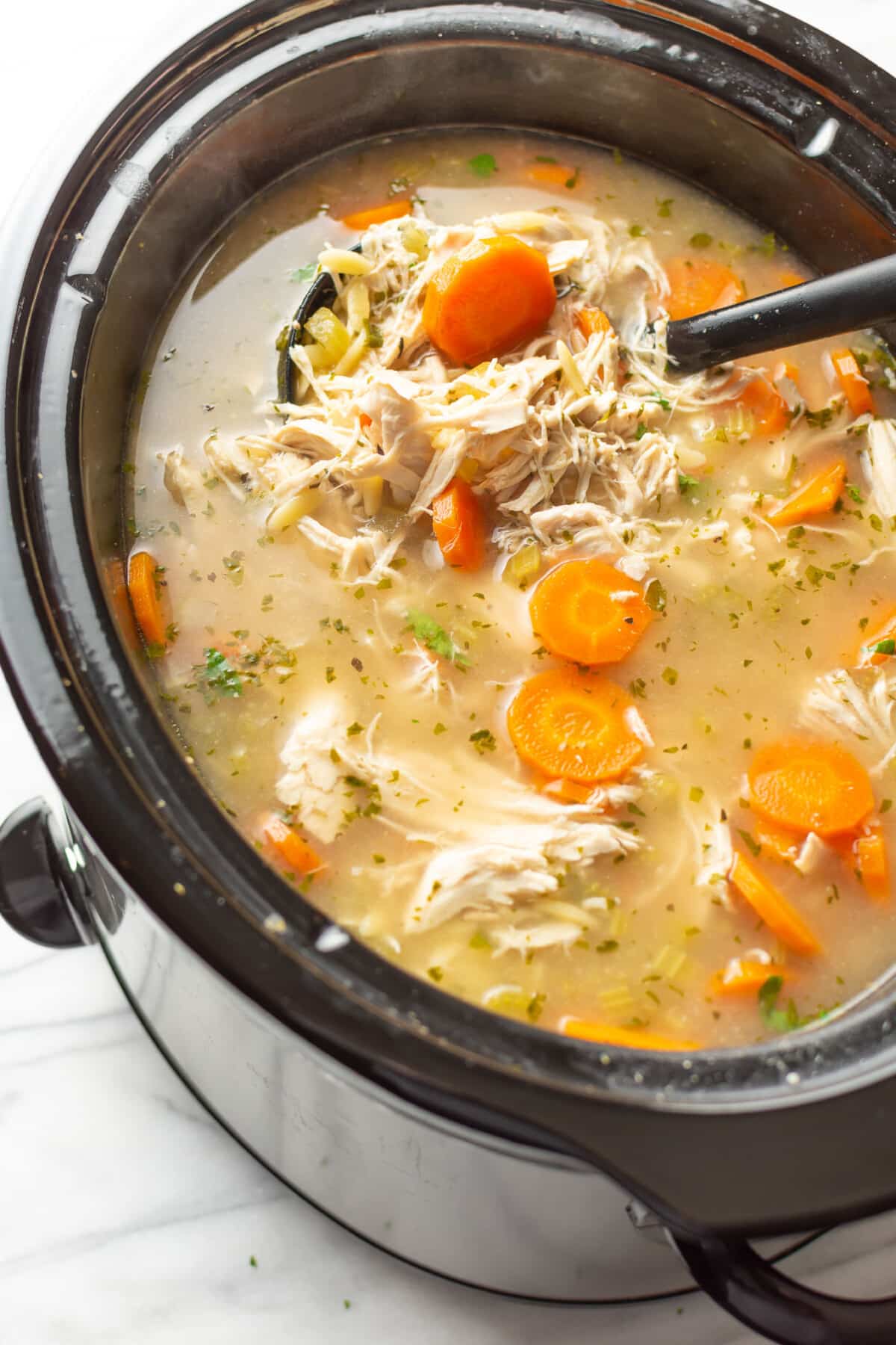 a slow cooker with lemon chicken orzo soup and a ladle