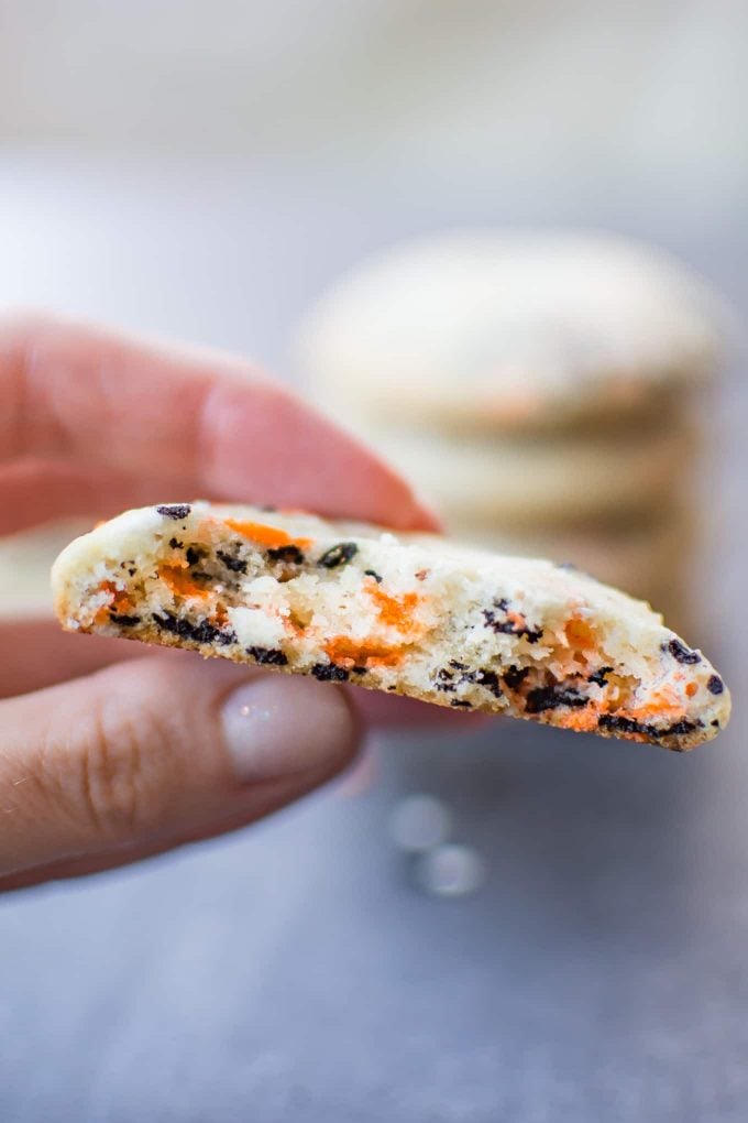 female hand holding half a Halloween sugar cookie with orange and black sprinkles