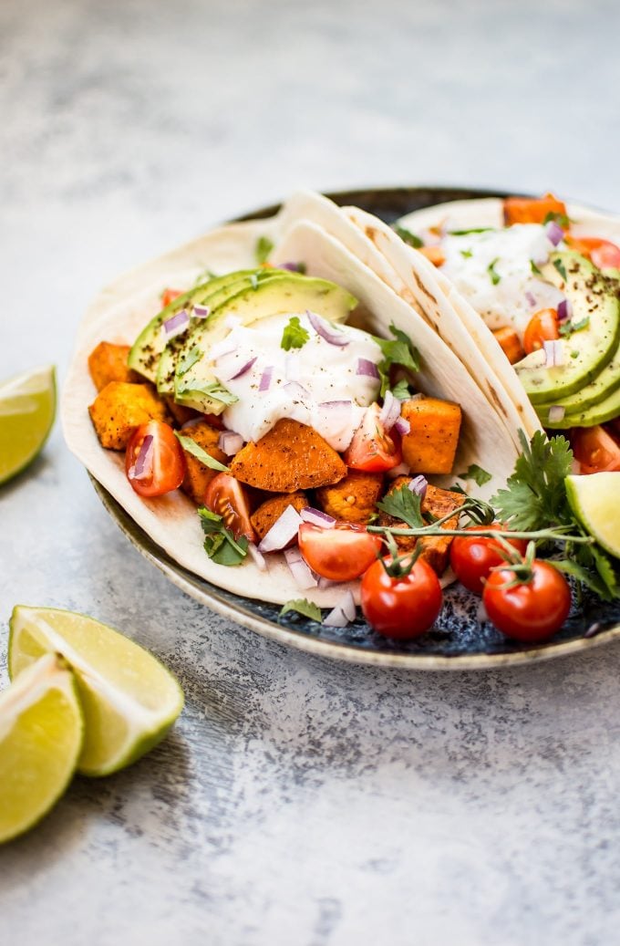 plate of vegetarian roasted sweet potato tacos on a plate with tomatoes and lime wedges