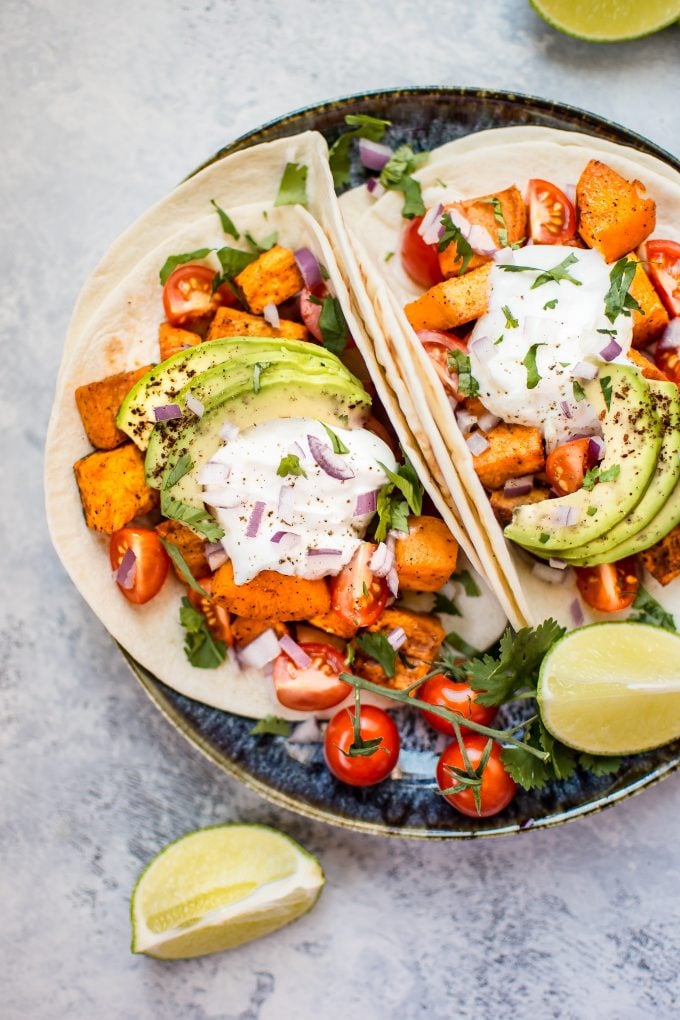 roasted sweet potato tacos on a plate beside little tomatoes and lime wedge