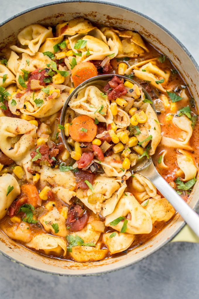 close-up of ladle with vegetarian tortellini soup with carrots and corn