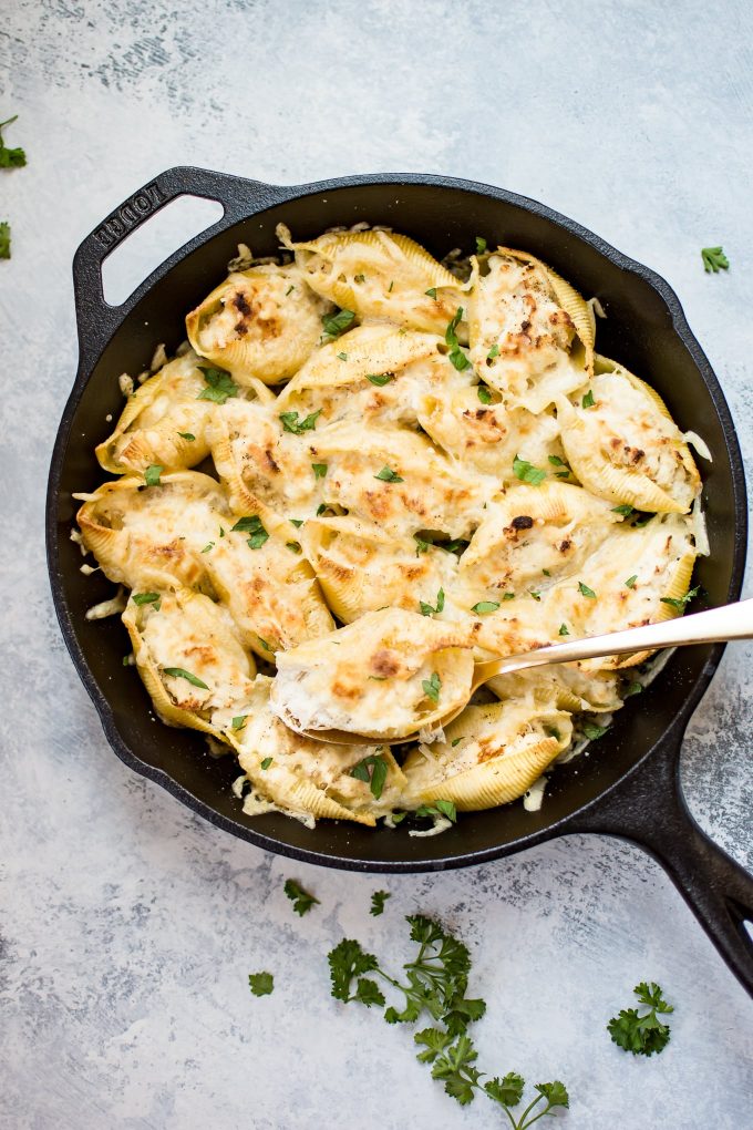cheesy chicken stuffed shells in a cast iron pan with serving spoon