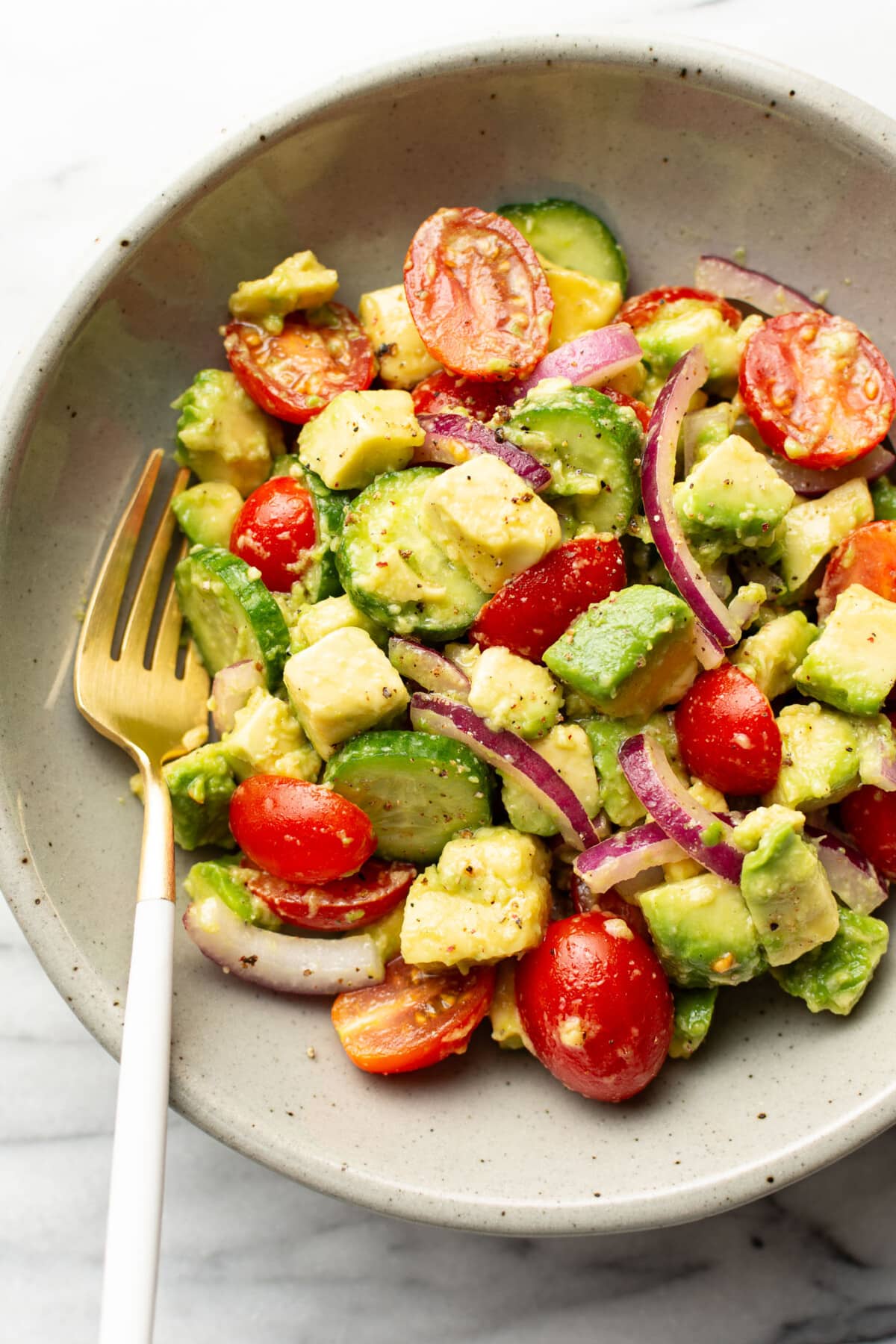 a bowl of cucumber tomato avocado salad with a fork