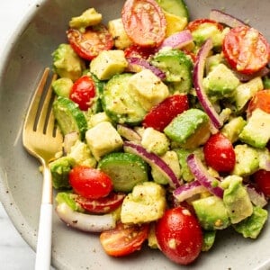 a bowl of cucumber tomato avocado salad with a fork