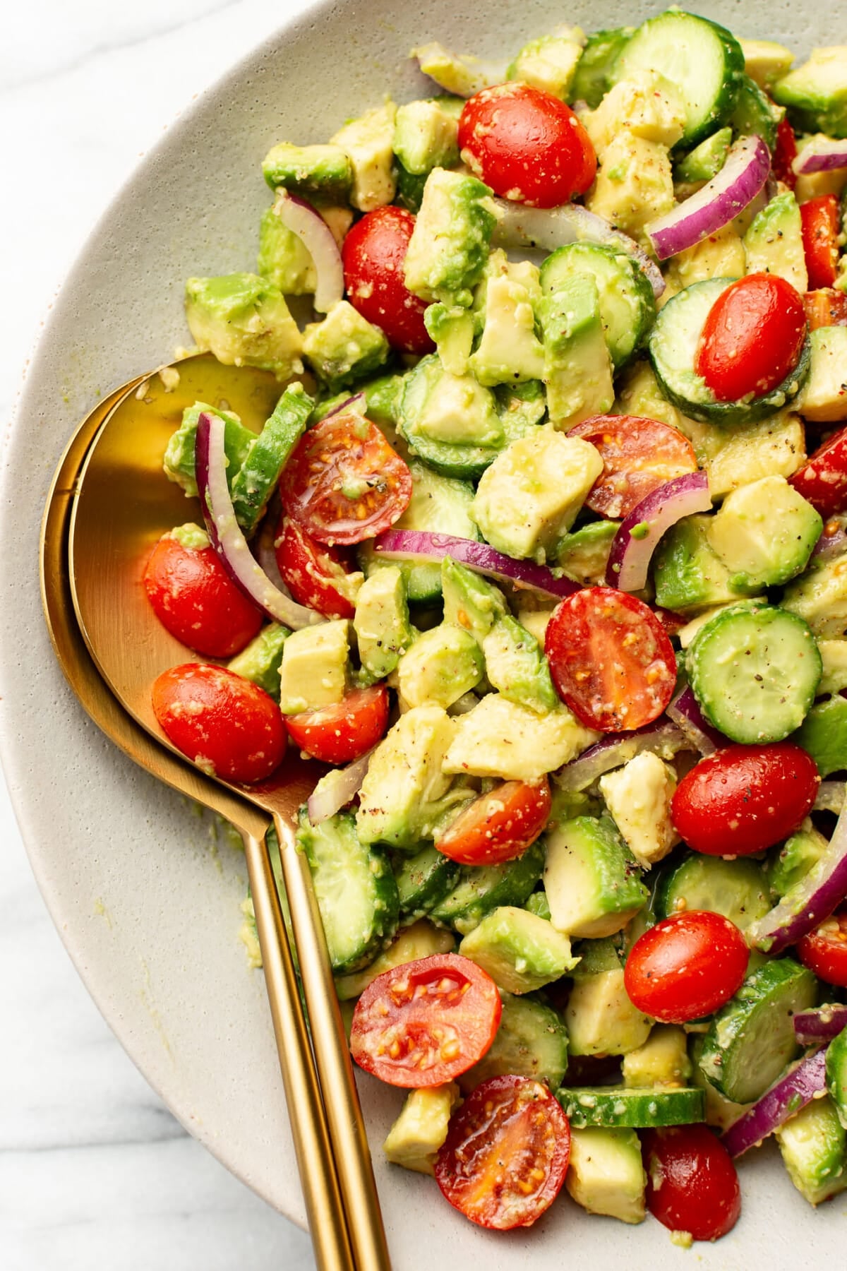 a bowl of cucumber tomato avocado salad with serving spoons