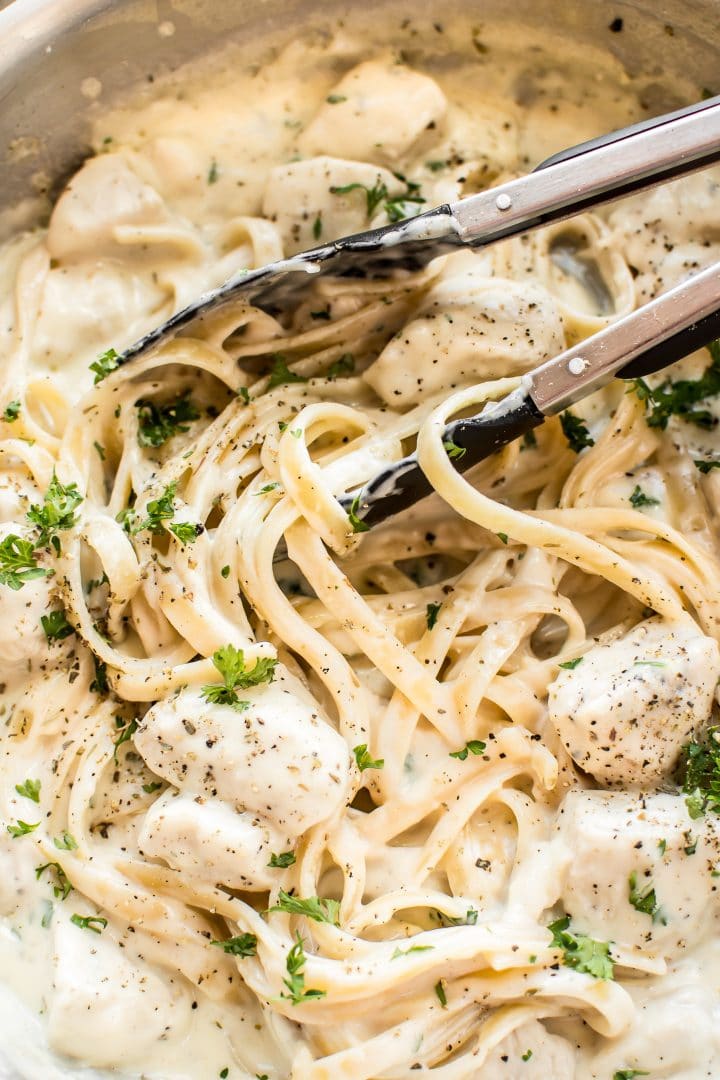 close-up of parmesan chicken alfredo with fettuccine and serving tongs