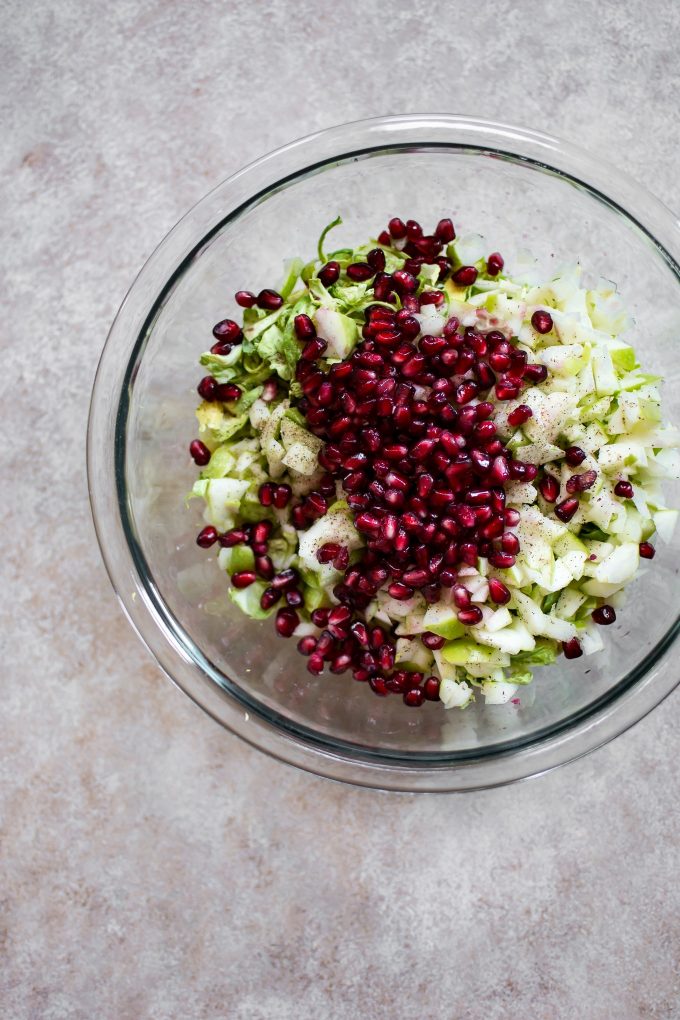 glass mixing bowl with ingredients for winter Brussels sprouts slaw