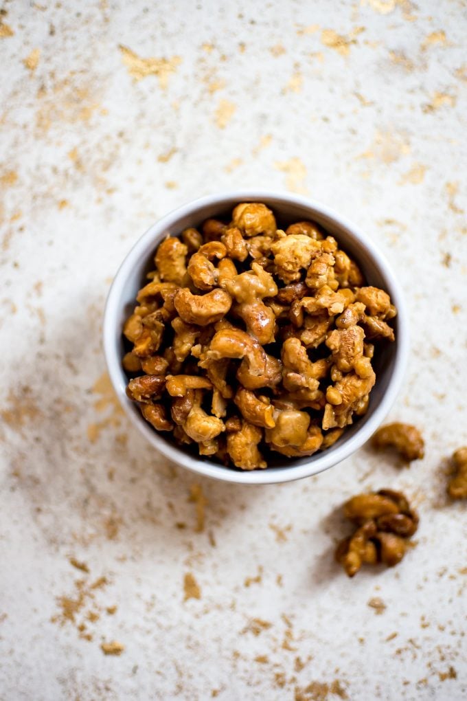 bowl of candied cashews with a few loose cashews beside it