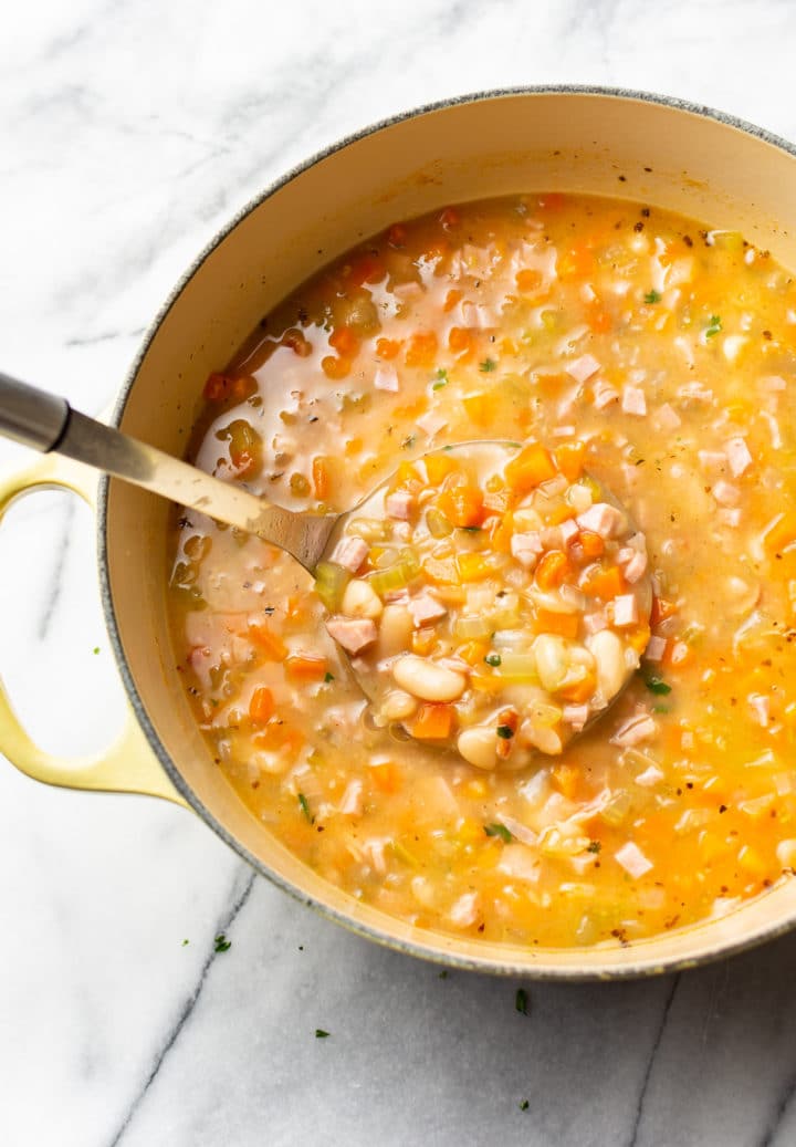 white bean and ham soup in a yellow pot with a ladle full