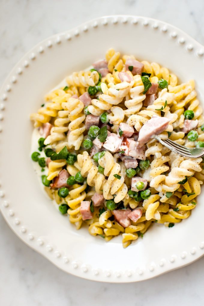 close-up of one pot ham and pea pasta in a white bowl with a fork