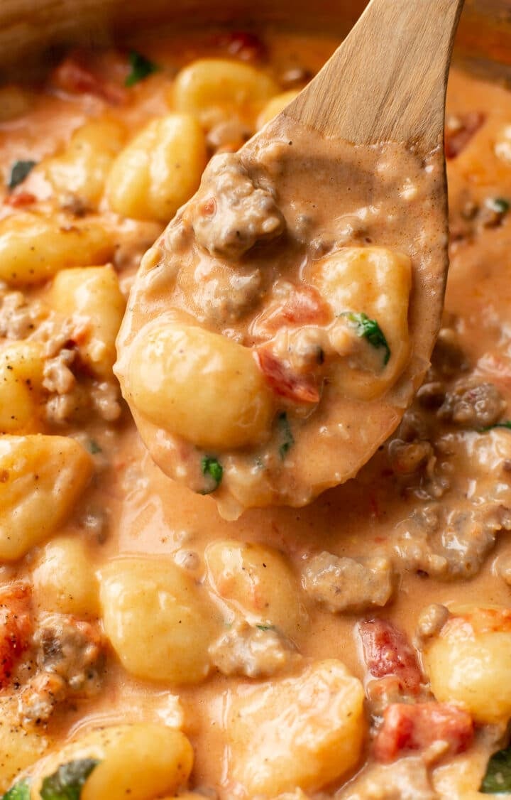 closeup of creamy gnocchi with sausage on a wooden spoon