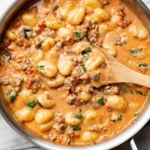 a skillet with italian sausage gnocchi and a wooden spoon