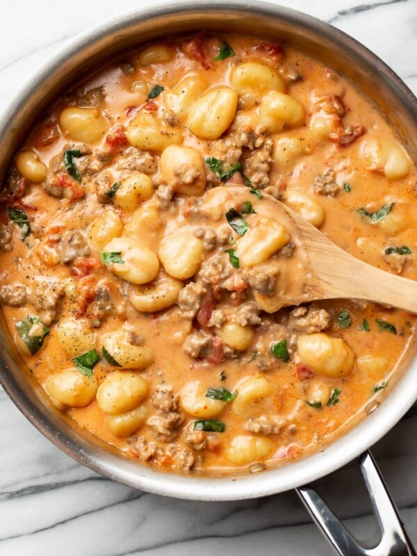 a skillet with italian sausage gnocchi and a wooden spoon