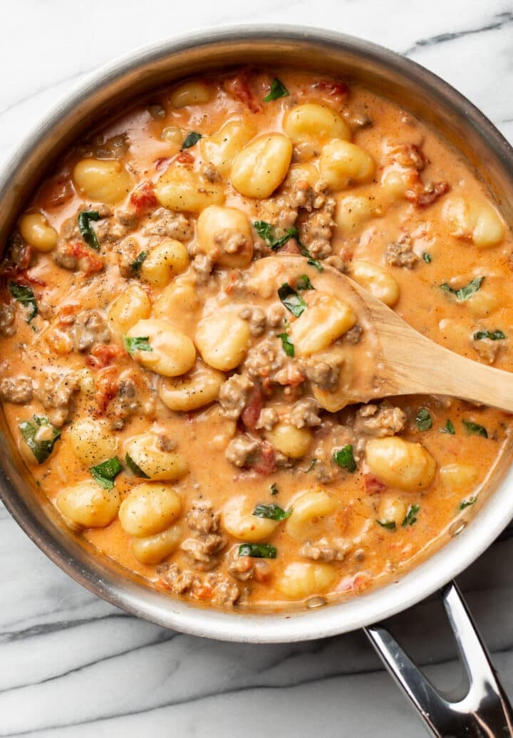a skillet with italian sausage gnocchi and a wooden spoon